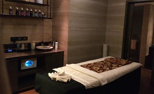 A luxurious spa room at Glamour Spa Islamabad featuring a massage bed, spa towels, essential oils on the table, and a sink beneath the table, creating a serene and relaxing ambiance for a soothing massage experience.